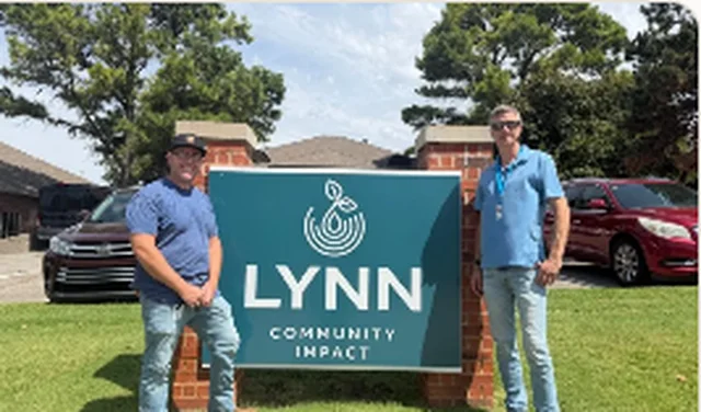 Two men standing beside the Lynn Community Impact entrance sign